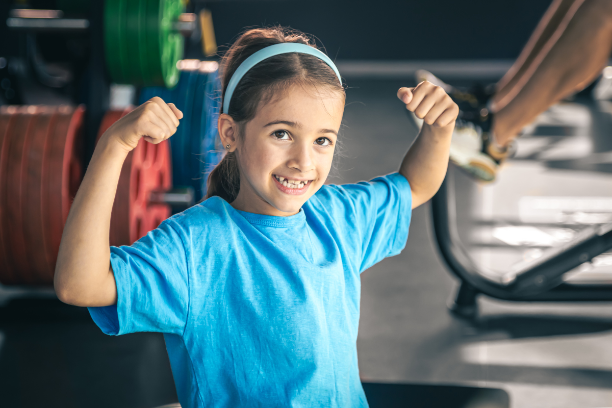 A young girl flexing her biceps at the gym in Texas.