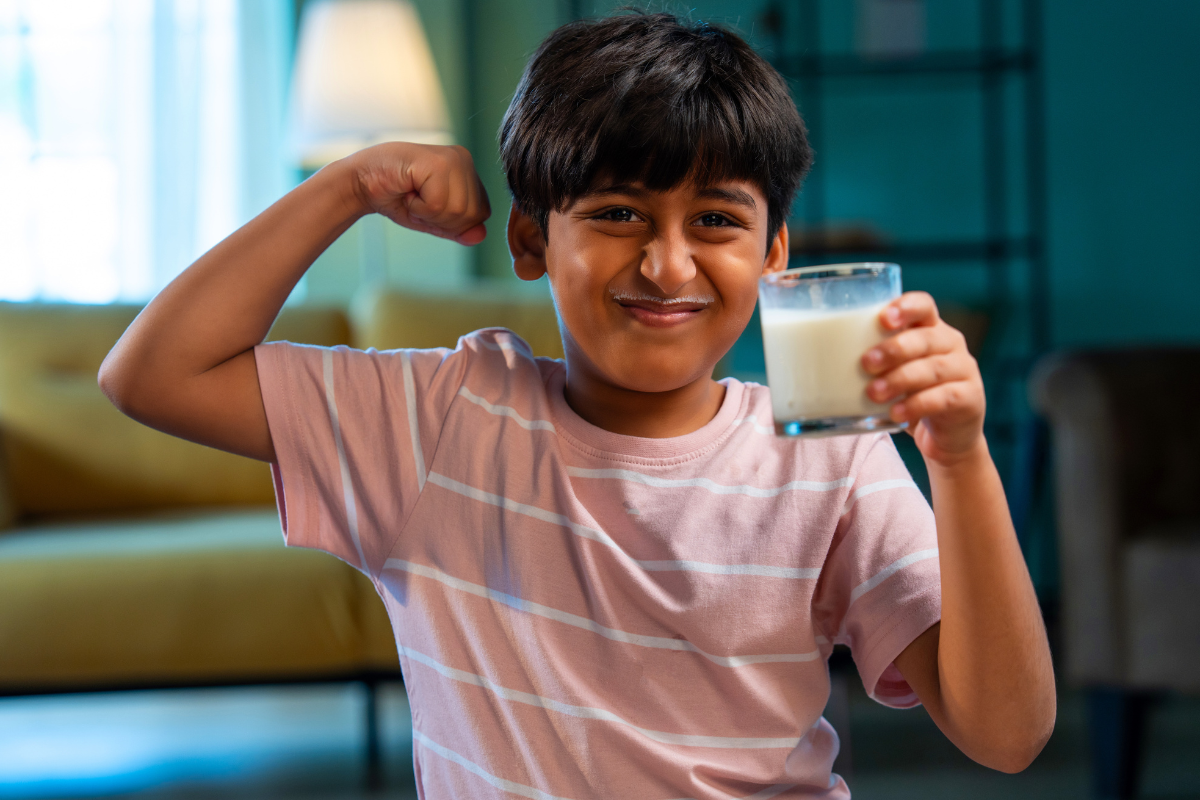 A smiling young boy holding a glass of milk and flexing his bicep, illustrating strong bones and healthy growth in Austin, Texas.